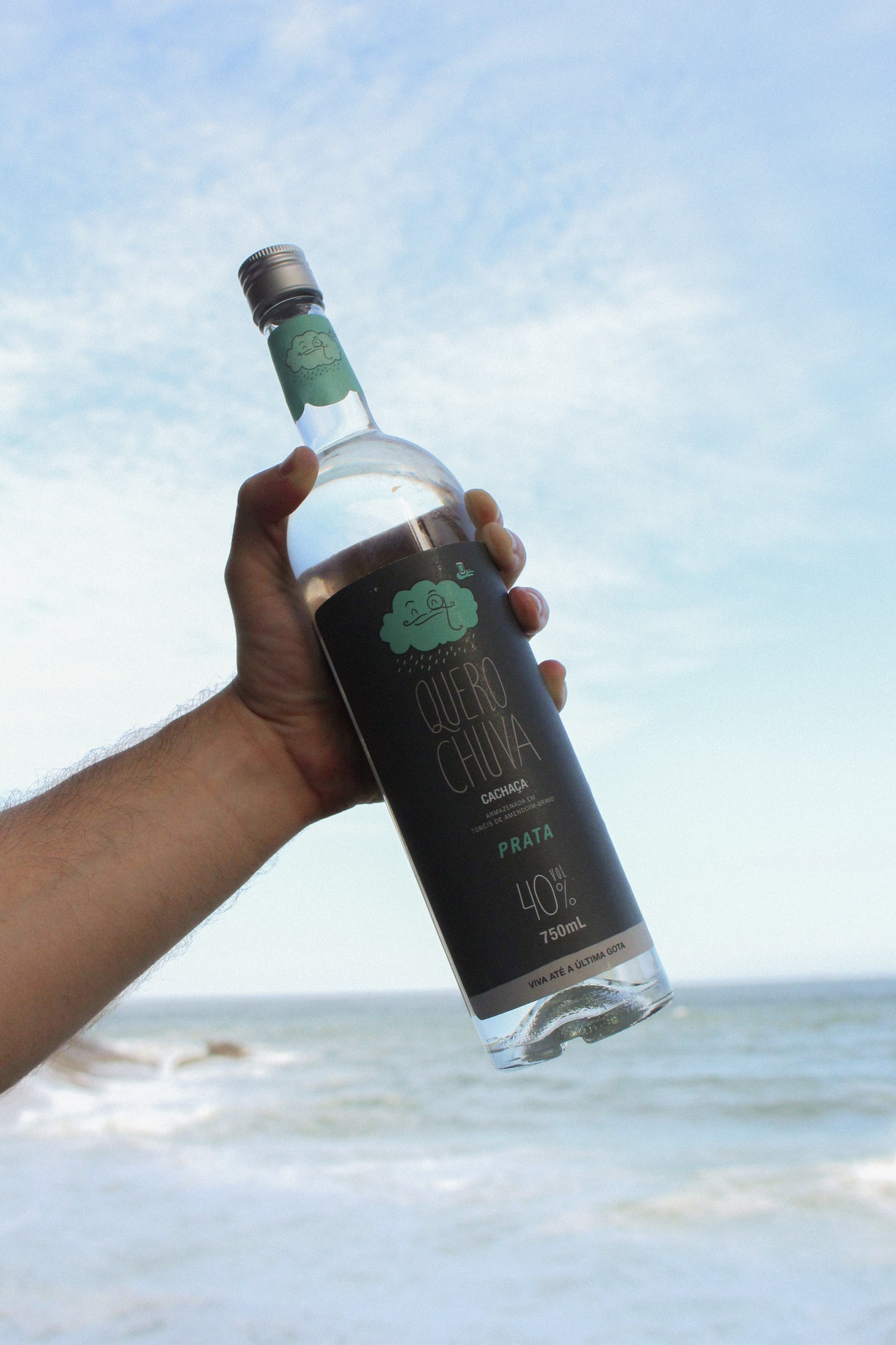 Mão erguendo garrafa Quero Chuva Prata 750 ml contra o céu
